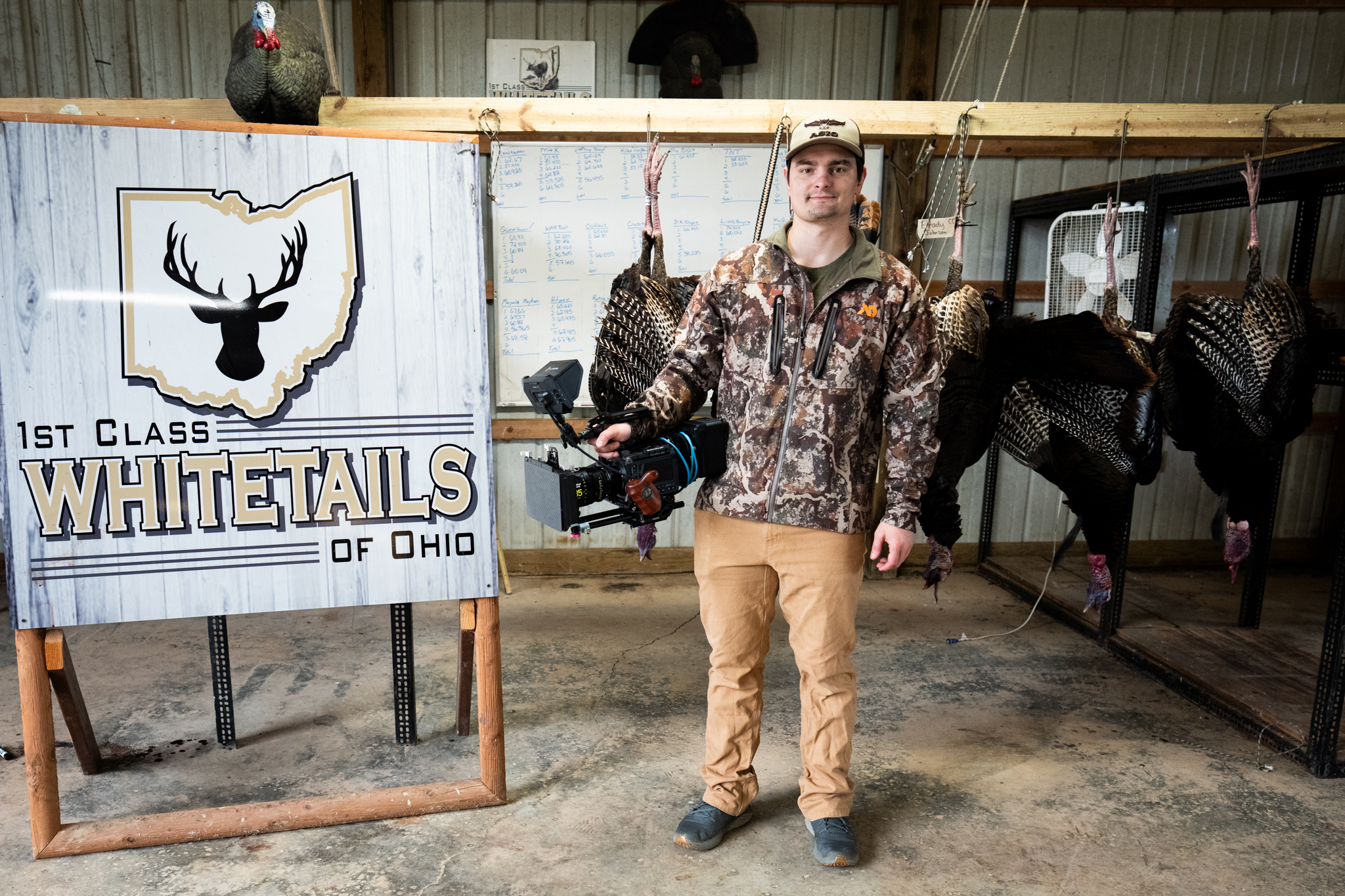 Sam Santa Rita on location at 1st Class Whitetails of Ohio holding a cinema camera, with harvested turkeys hanging in the background.